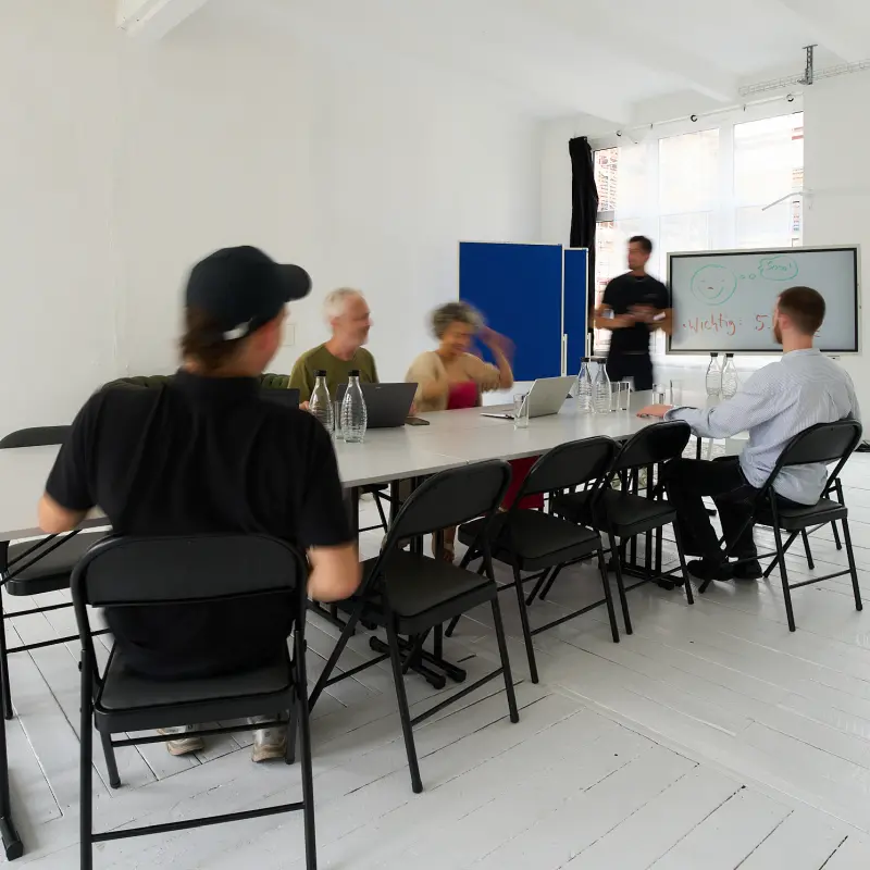 training-800 Mehrere Menschen sind in einem hellen Raum in einem Business Training bei Meeet, eine Person erläutert etwas an einem elektronischen Flipchart.
